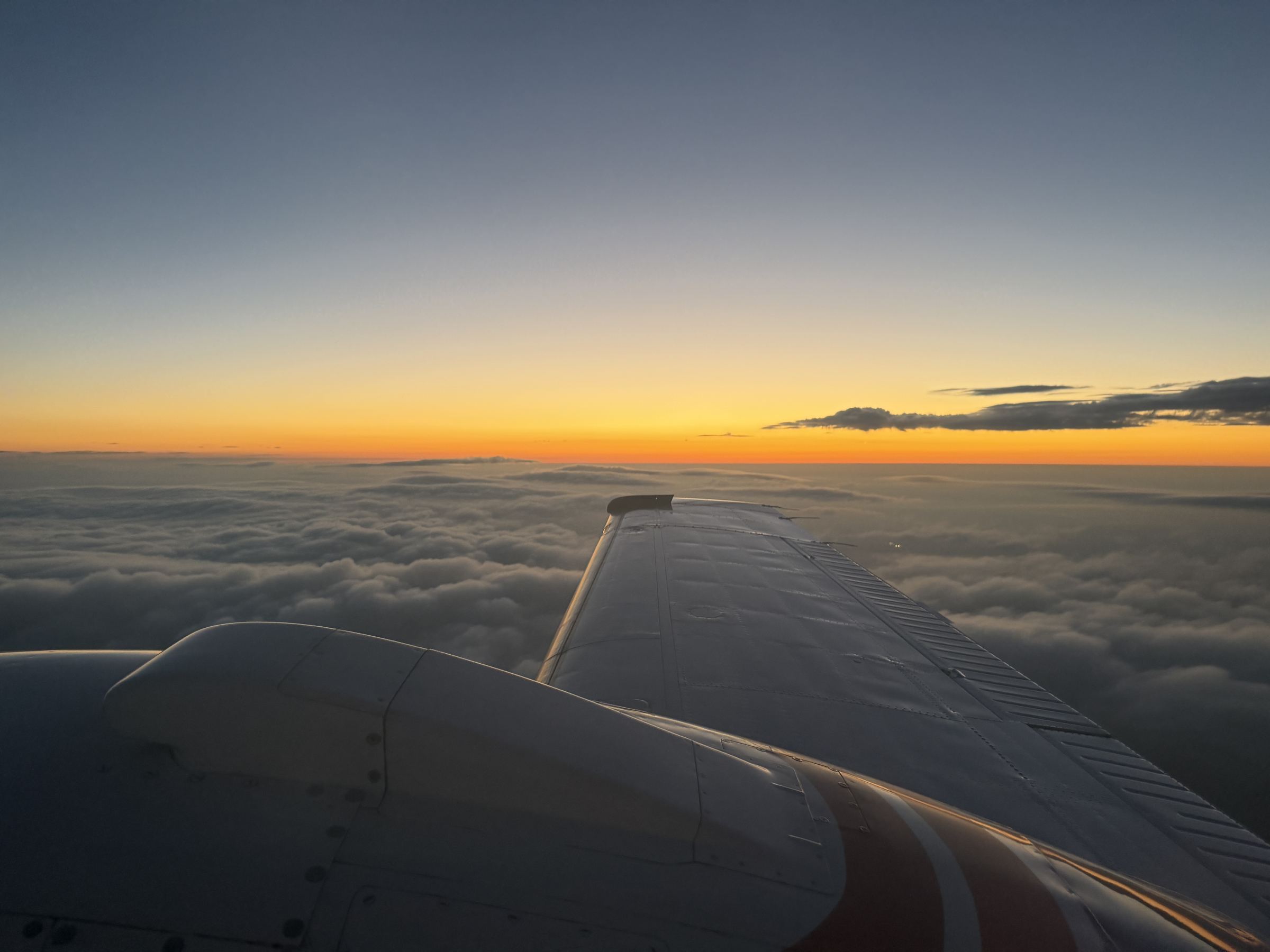 A piston twin's wing over a cloud deck at dusk